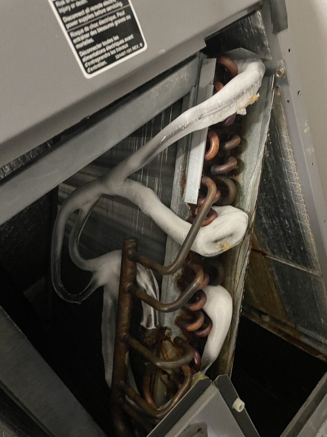 A close-up view of an HVAC evaporator coil with ice buildup on copper tubes and fins inside the metal housing—an issue an HVAC contractor often encounters during system diagnostics.