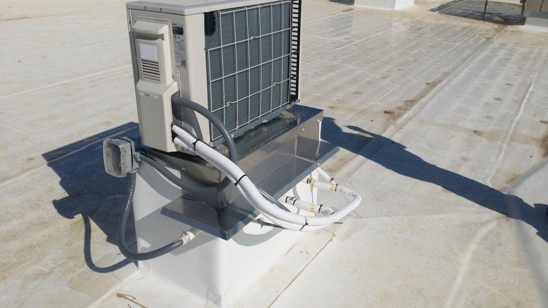 An outdoor air conditioning unit installed on a rooftop by a professional HVAC contractor, with insulated pipes and electrical wiring connected.