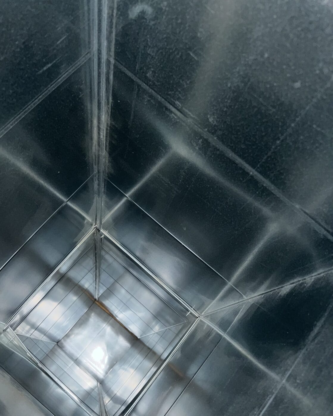 View inside a reflective, empty metal container with a grid-like light pattern visible at the bottom.