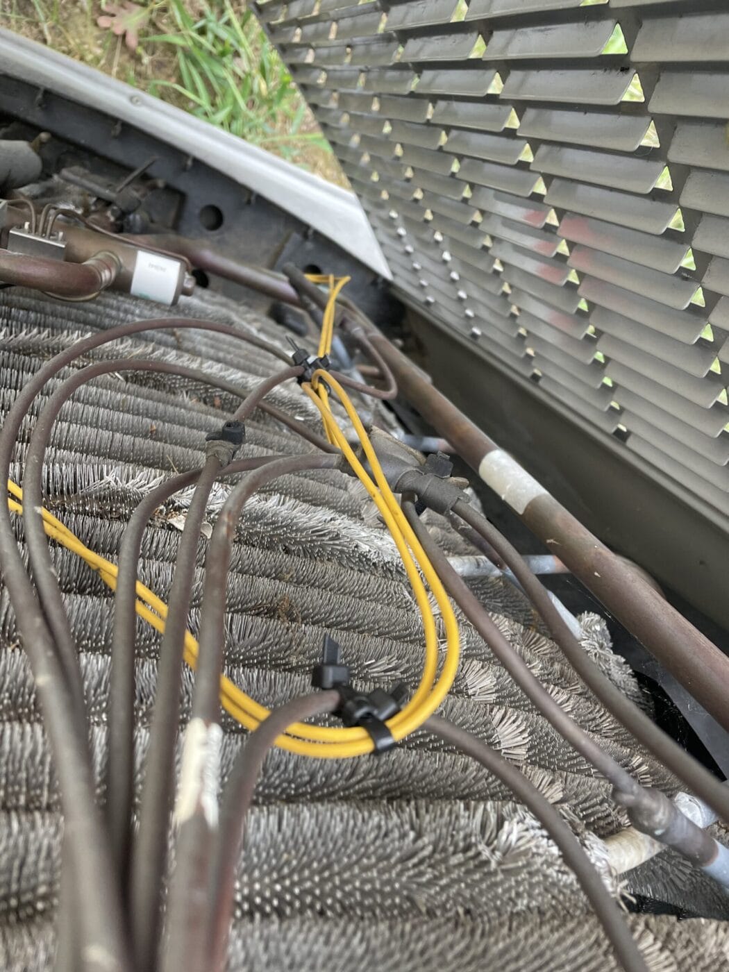 Close-up of the interior of an air conditioning unit showing metal coils, wires, and components with a perforated cover partially open.