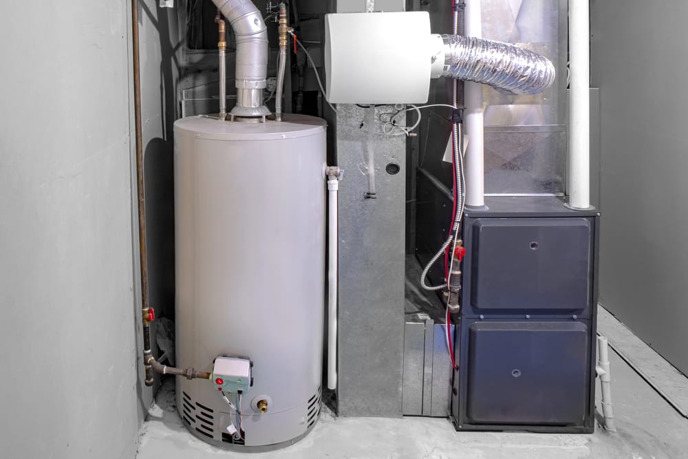 A water heater and a furnace installed side by side in a basement utility area, with visible metal pipes and ductwork—expertly set up by an experienced HVAC contractor.